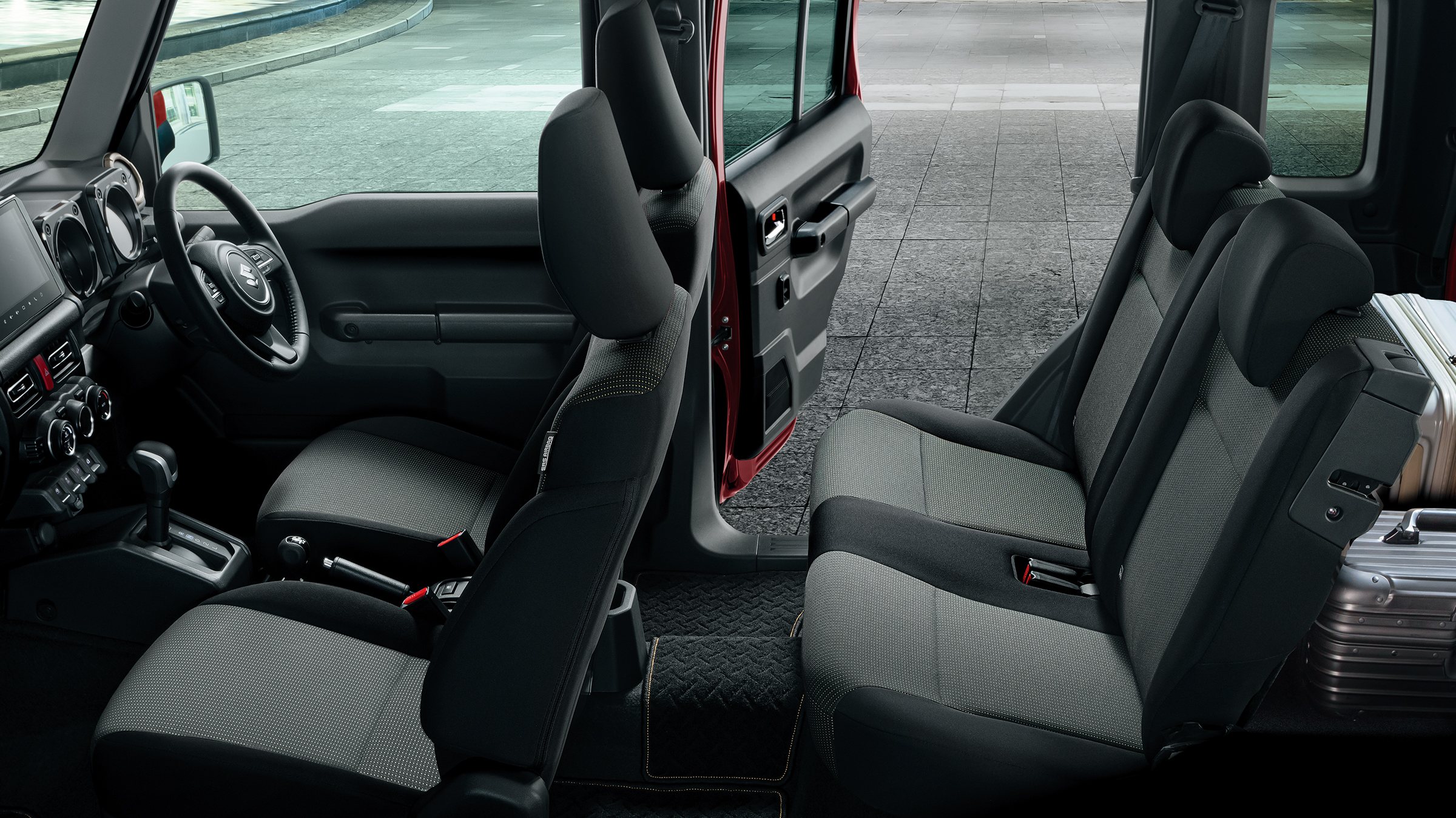ภายใน Suzuki Jimny Nomade มองจากด้านข้าง เห็นเบาะหน้า ประตูหลังที่เปิดอยู่ เบาะแถวหลัง และกระเป๋าเดินทางวางข้างเบาะ