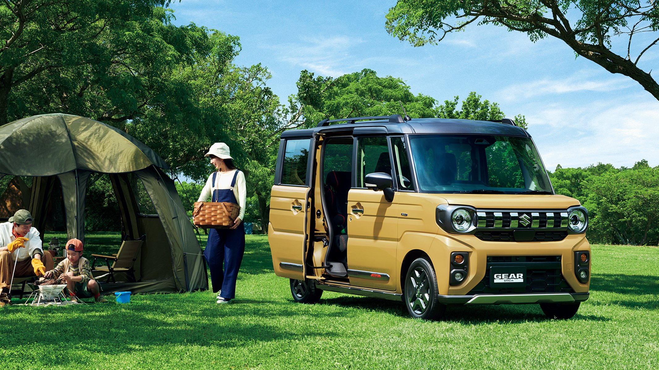 รถ Suzuki Spacia Gear สีเหลืองมัสตาร์ดเปิดประตูสไลด์ จอดบนสนามหญ้า มีครอบครัวตั้งแคมป์อยู่ด้านข้าง